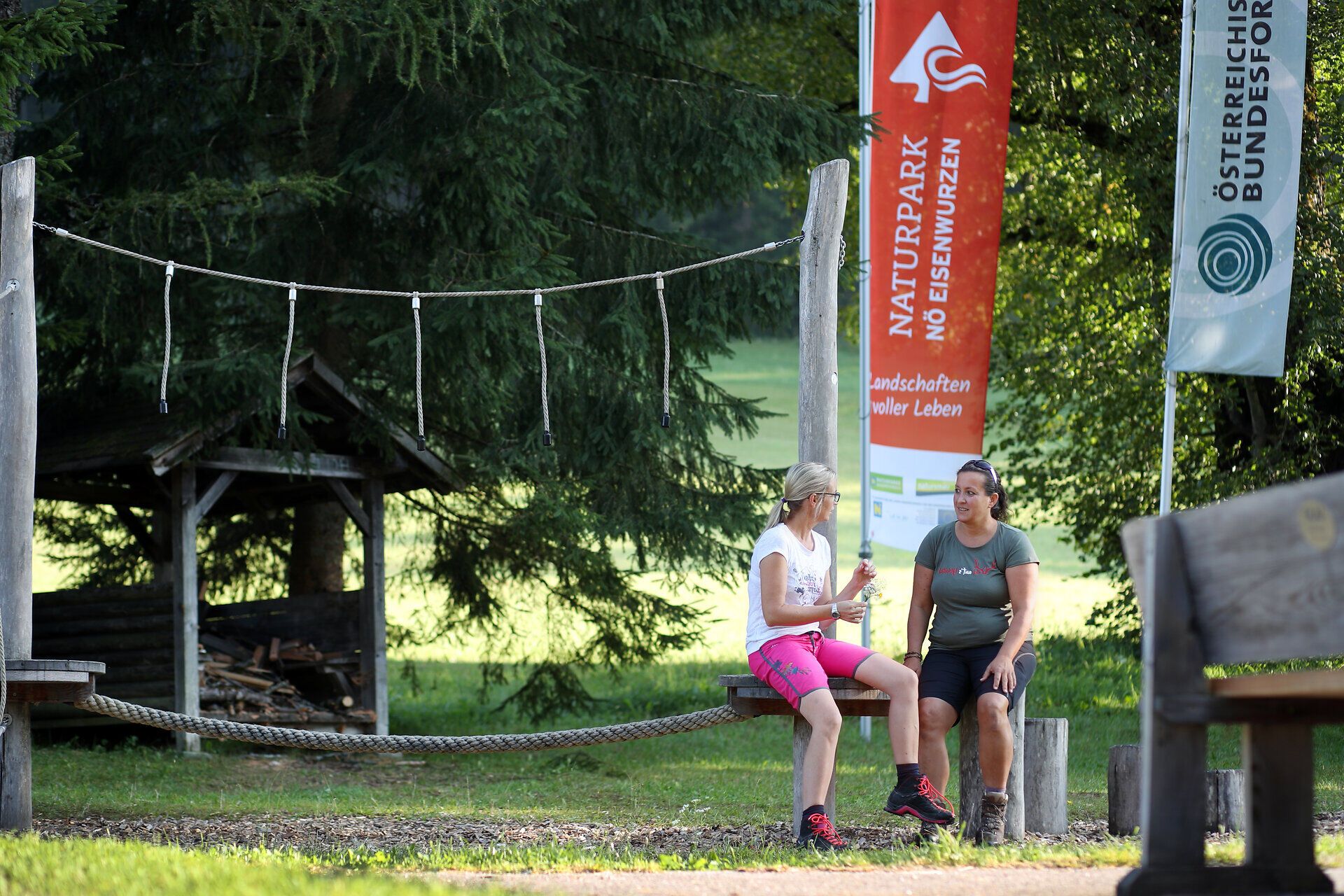 Zwei Frauen sitzen auf Spielgeräten am Spielplatz Promau und unterhalten sich. 