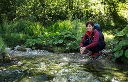 Pilgerin kniet am Bach im Wald.