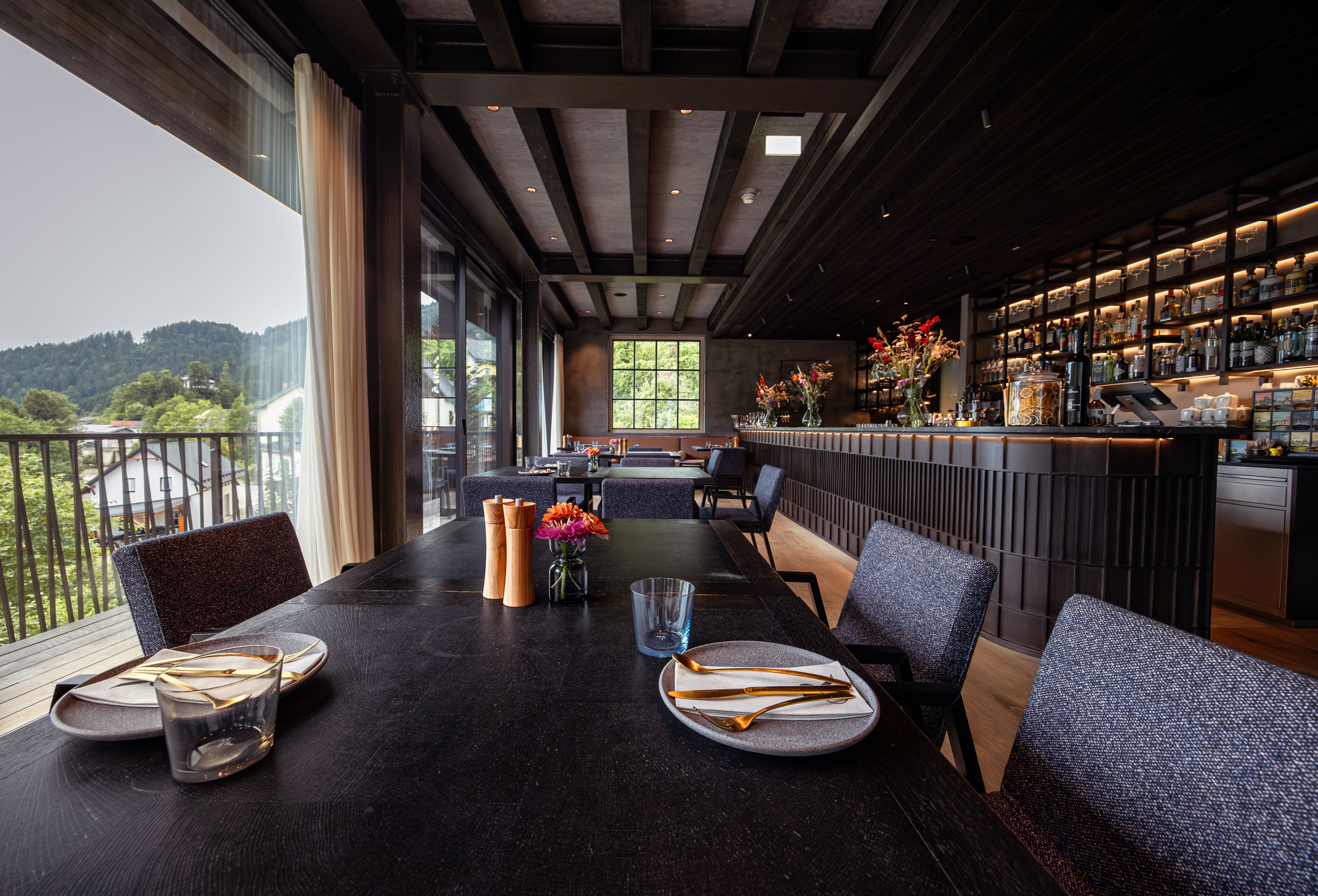 Innenansicht eines modernen Restaurants mit gedecktem Tisch und Bar im Hintergrund.