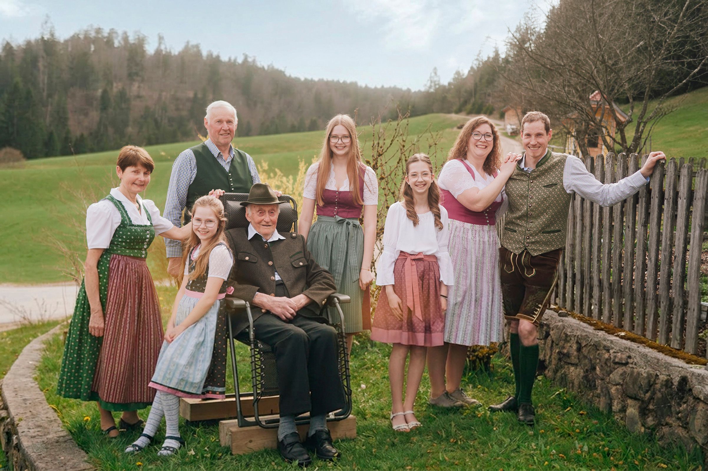 Eine Familie in traditioneller Tracht posiert im Freien vor einer ländlichen Kulisse mit Wiesen und Bäumen.