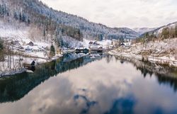 Die winterliche Landschaft um den See verzaubert mit einer schimmernden Schneedecke, die die umliegenden Berge sanft umhüllt. Die ruhige Wasseroberfläche spiegelt die majestätische Kulisse wider und lädt zu einem besinnlichen Spaziergang ein.