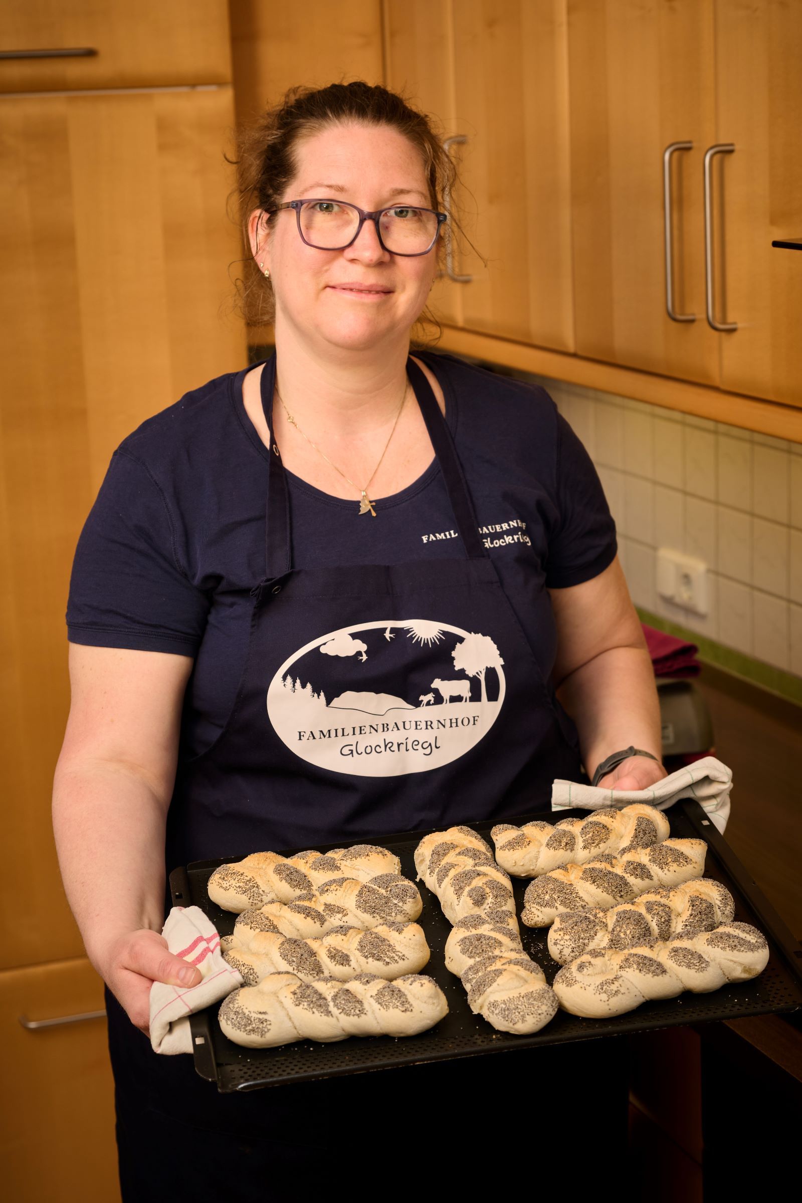 Eine Frau in einer Küche hält ein Blech mit frisch gebackenen Mohnbrötchen.