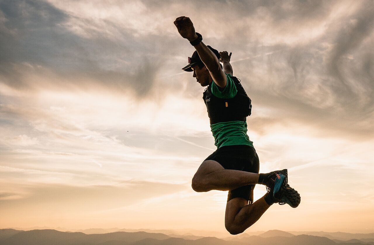 Ein Trailrunner springt voller Energie über die Berglandschaft, während die goldenen Sonnenstrahlen den Horizont erleuchten. Die frische, klare Luft und die atemberaubende Aussicht laden dazu ein, die Schönheit des Bergsommers in vollen Zügen zu genießen.