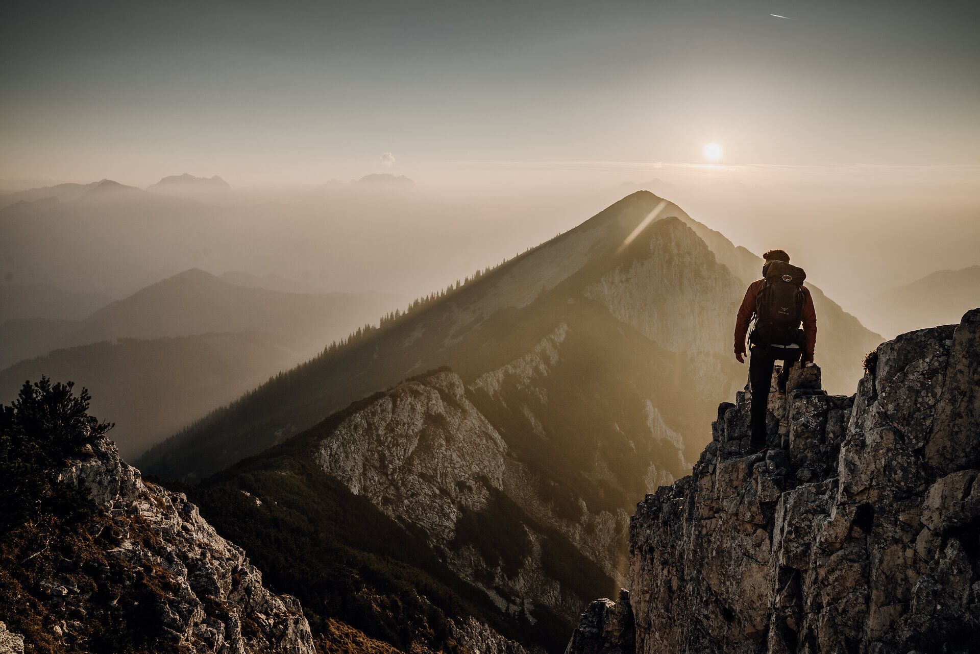 Ein Wanderer steht am Rand eines majestätischen Berggipfels und blickt auf die sanften Hügel und Täler der Ybbstaler Alpen. Die goldenen Strahlen der untergehenden Sonne tauchen die Landschaft in ein warmes Licht und schaffen eine friedliche Atmosphäre, die zum Verweilen einlädt. Hier, inmitten der Natur, entfaltet sich die Schönheit des Bergsommers in voller Pracht.