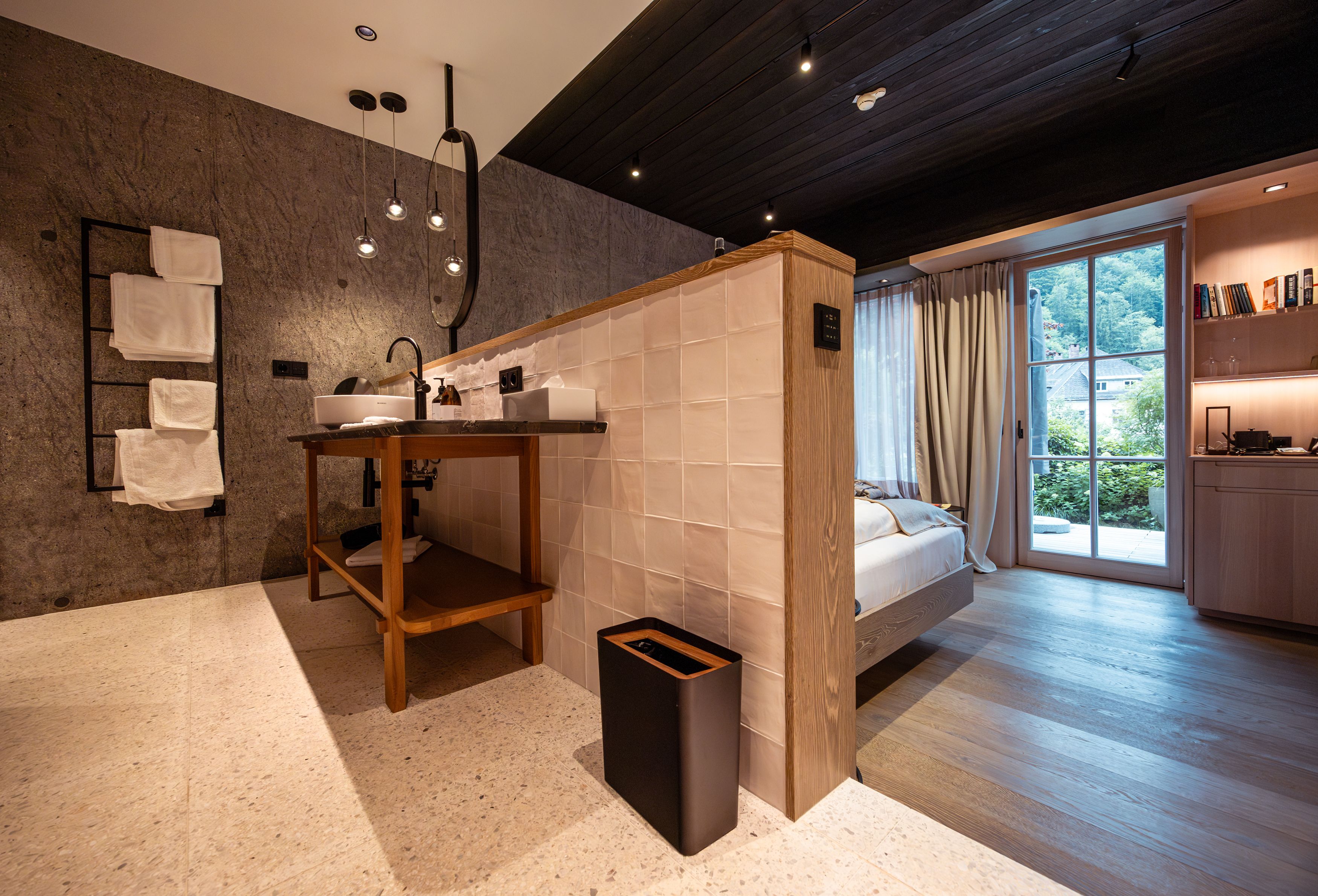 Modernes Hotelzimmer mit offenem Badezimmer, Holzboden und großen Fenstern mit Blick ins Grüne.