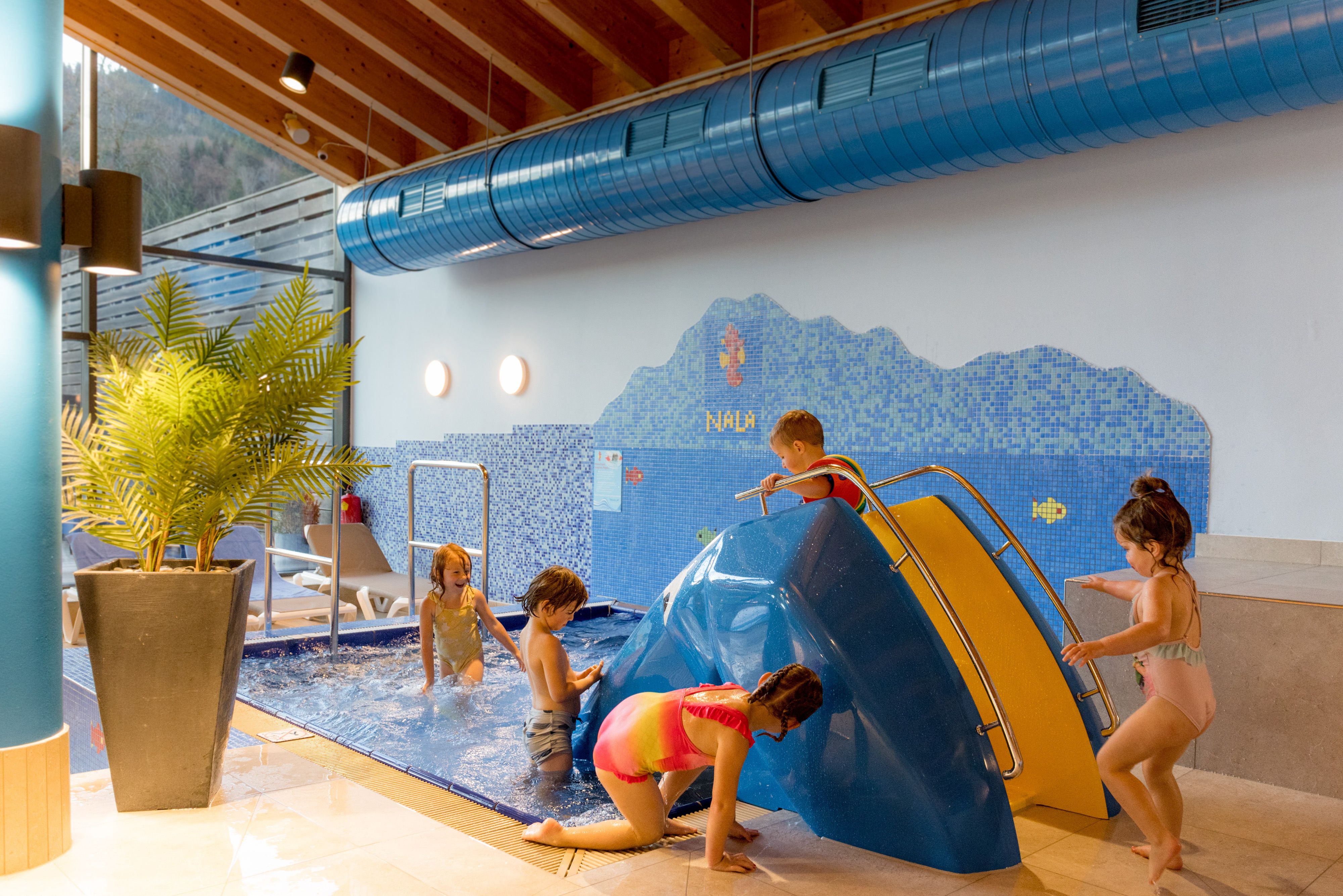 Kinder spielen in einem Innenpool mit einer kleinen Rutsche im Ybbstaler Solebad.