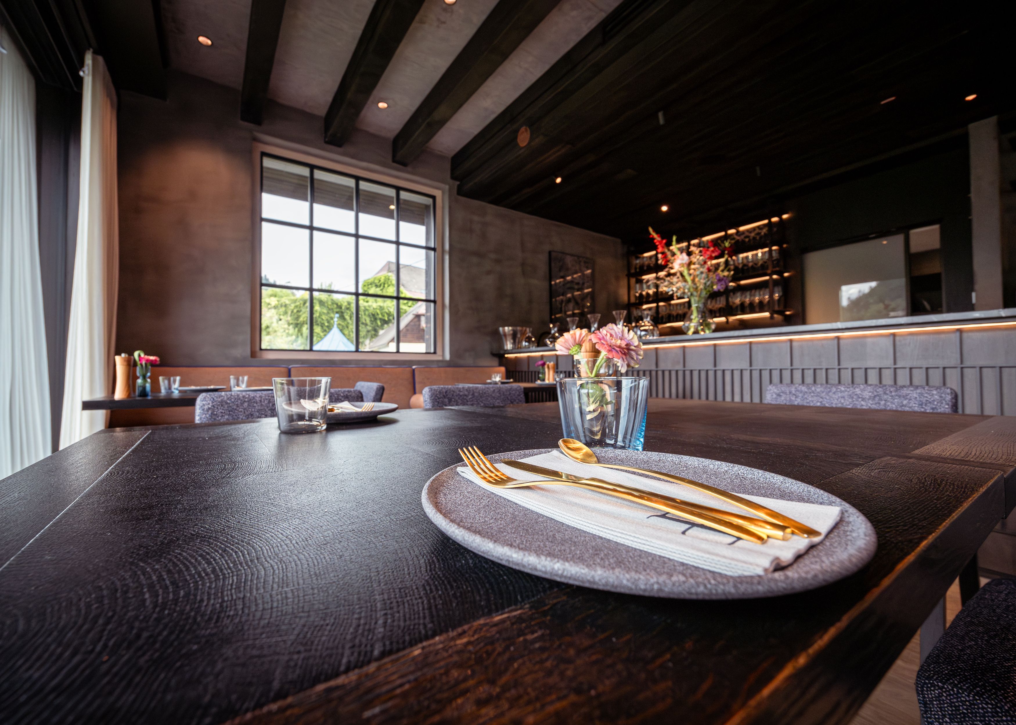 Elegantes Restaurant mit gedecktem Tisch, goldfarbenem Besteck und Blumen.