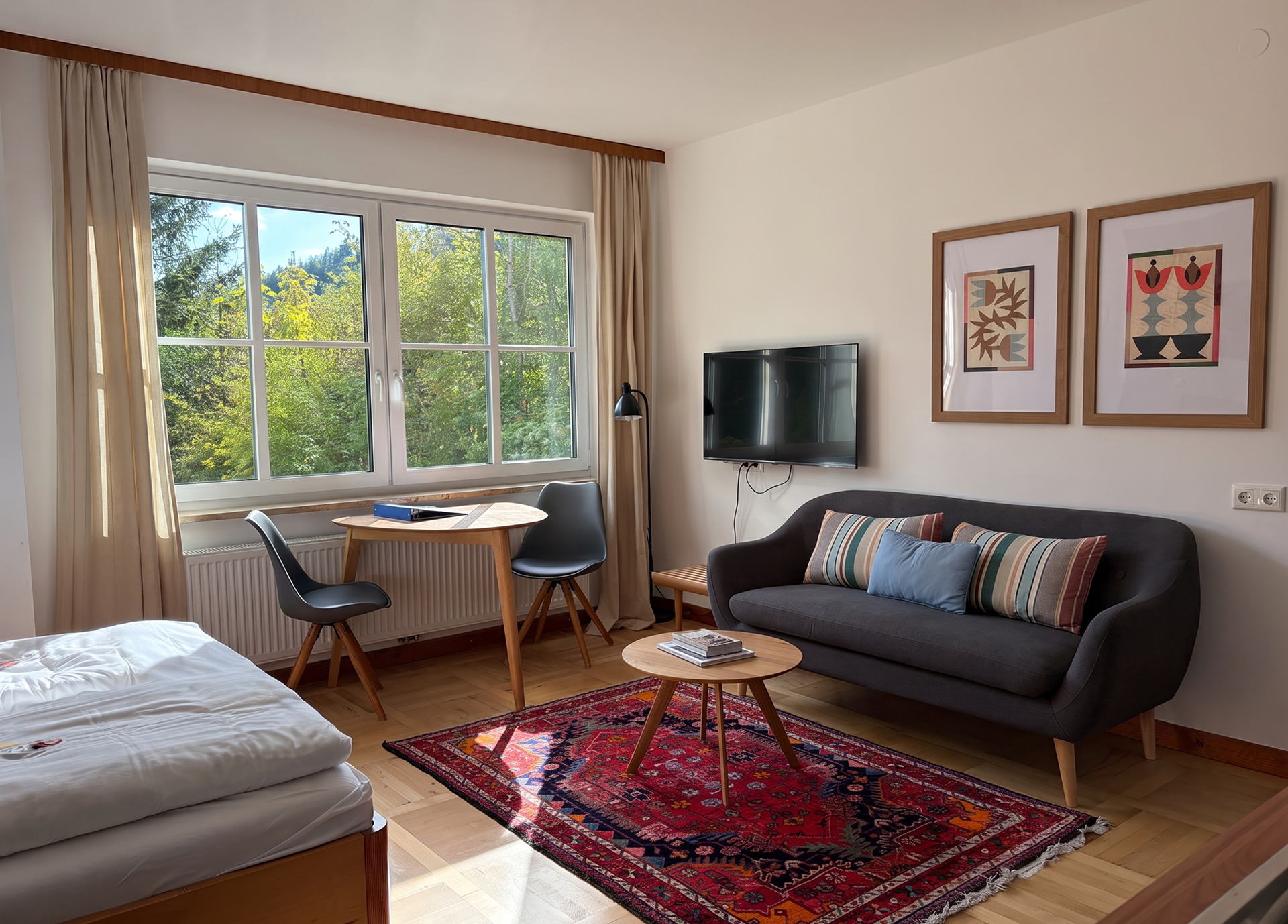 Gemütliches Wohnzimmer mit Sofa, Tisch, Stühlen und großem Fenster mit Blick ins Grüne.