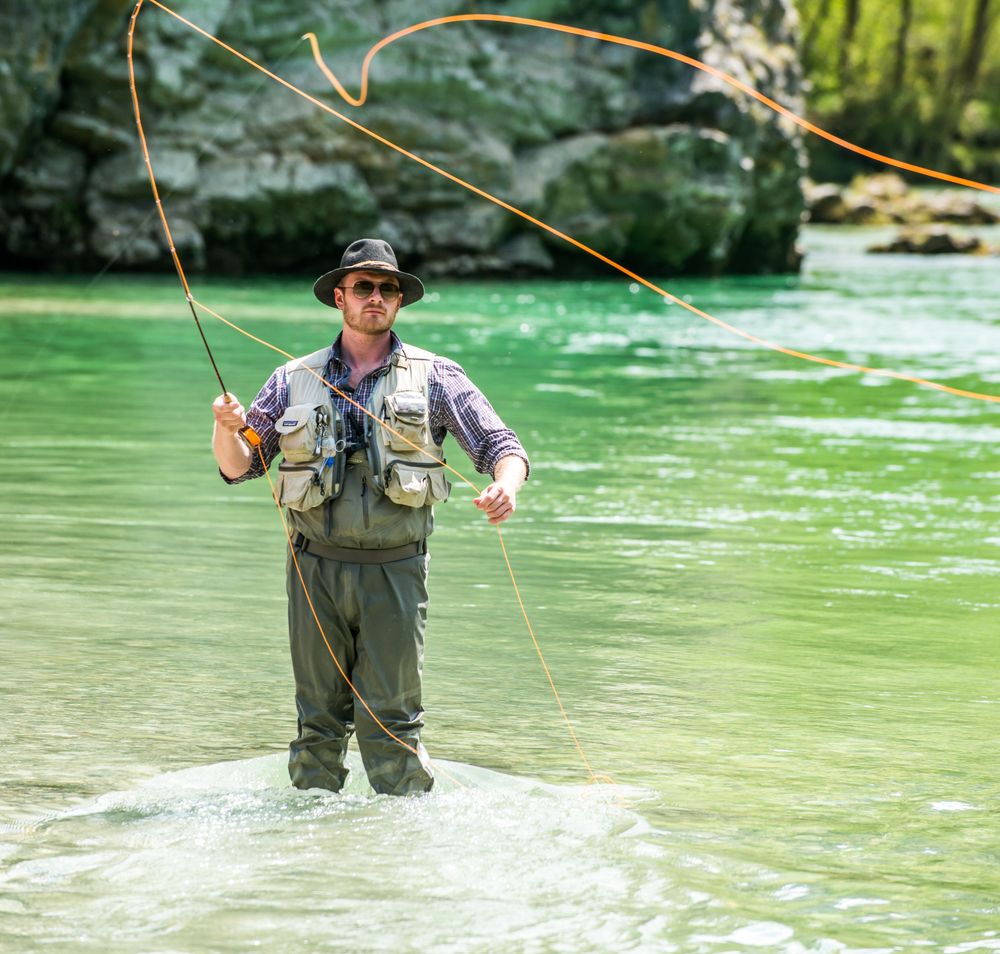 Ein Mann beim Fliegenfischen in einem Fluss, mit einem springenden Fisch im Vordergrund.