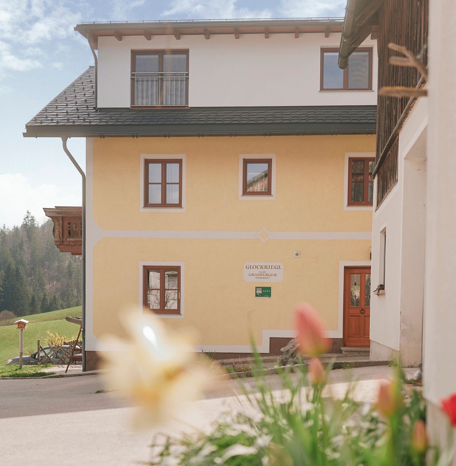 Gelbes Haus mit Holzbalkon und Blumen im Vordergrund.