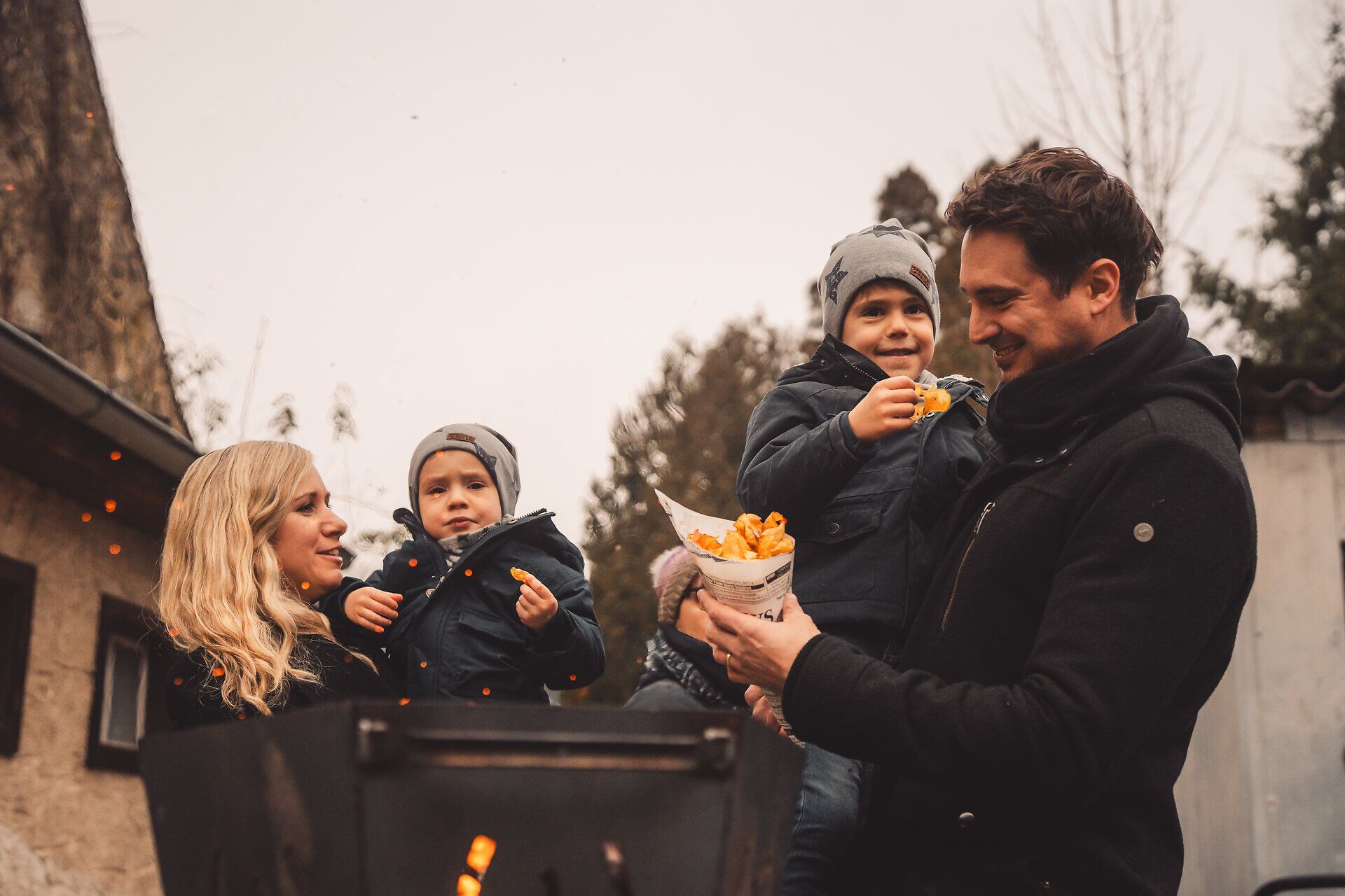 Familie wärmt sich am Feuerkorb und verkostet regionale Spezialitäten.